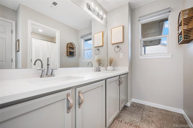 bathroom featuring double vanity, a sink, visible vents, and baseboards