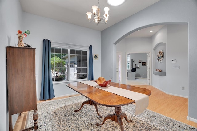 dining space featuring arched walkways, a chandelier, light wood-style flooring, and baseboards