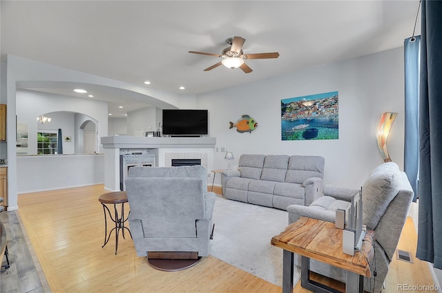 living room with ceiling fan, a tiled fireplace, and light hardwood / wood-style flooring