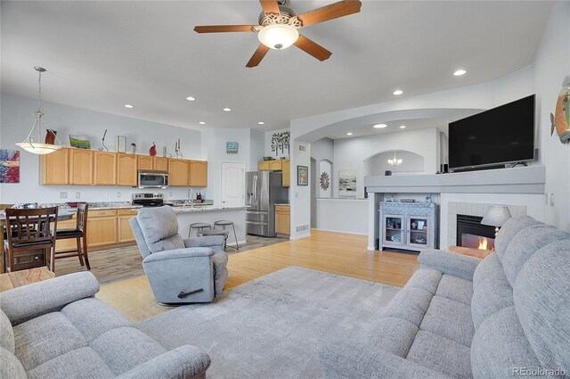 living room featuring ceiling fan, a tiled fireplace, light hardwood / wood-style floors, and sink