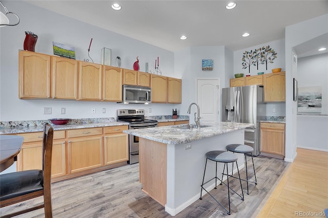 kitchen with stainless steel appliances, light hardwood / wood-style floors, a kitchen island with sink, and sink