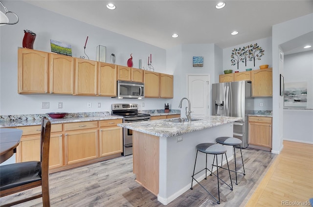 kitchen featuring light wood-style flooring, appliances with stainless steel finishes, light brown cabinets, a sink, and a kitchen breakfast bar