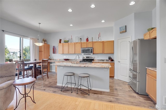 kitchen with an island with sink, light wood finished floors, stainless steel appliances, and light brown cabinetry