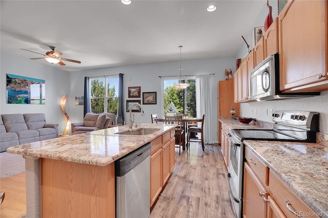 kitchen featuring stainless steel appliances, open floor plan, a kitchen island with sink, a sink, and light wood-type flooring