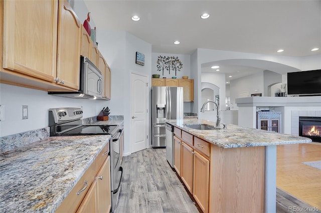 kitchen with a fireplace, light hardwood / wood-style flooring, sink, light stone countertops, and appliances with stainless steel finishes