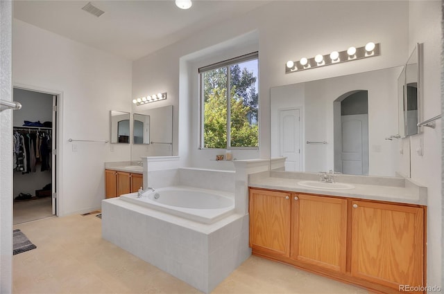 bathroom with a garden tub, visible vents, two vanities, and a sink