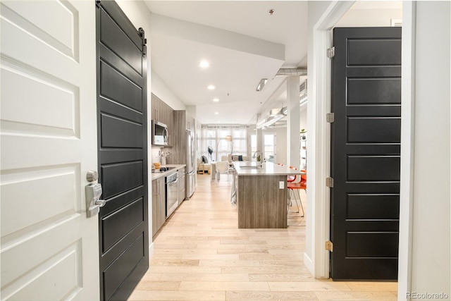 kitchen featuring sink, a center island with sink, appliances with stainless steel finishes, a barn door, and light hardwood / wood-style floors