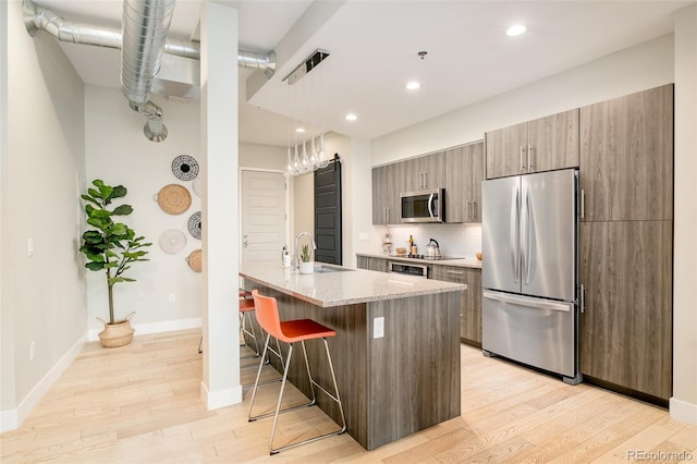 kitchen with a breakfast bar, pendant lighting, sink, stainless steel appliances, and light stone countertops