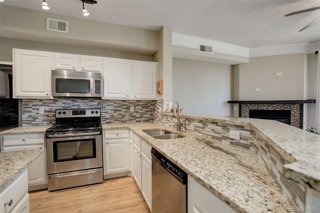 kitchen with sink, appliances with stainless steel finishes, light stone counters, light hardwood / wood-style floors, and white cabinets