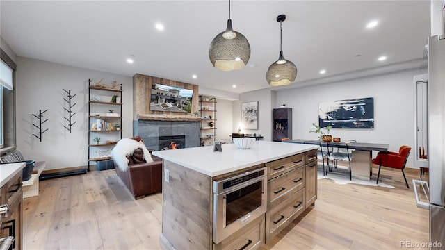 kitchen featuring a tiled fireplace, a kitchen island, hanging light fixtures, and light wood-type flooring