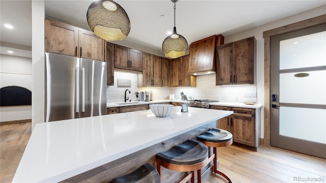 kitchen with a kitchen breakfast bar, light wood-type flooring, sink, stainless steel refrigerator, and hanging light fixtures