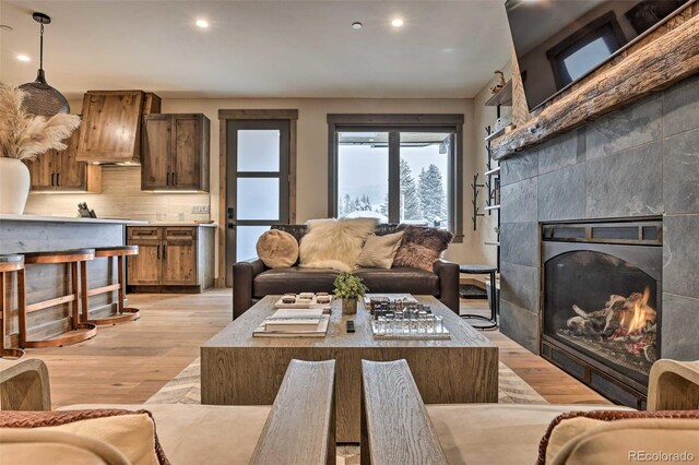 living room with a tiled fireplace and light wood-type flooring