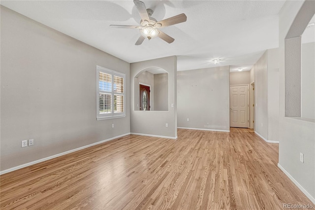 empty room with baseboards, light wood-style floors, ceiling fan, and arched walkways