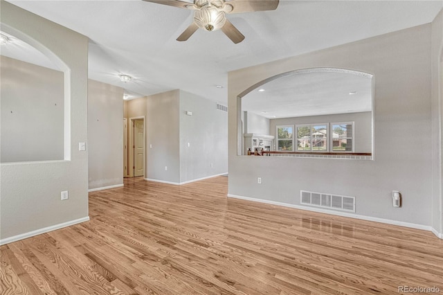 unfurnished living room featuring a ceiling fan, wood finished floors, visible vents, baseboards, and arched walkways