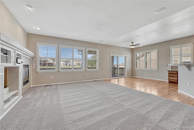 unfurnished living room with baseboards, ceiling fan, a textured ceiling, a tiled fireplace, and light colored carpet