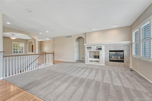 unfurnished living room with visible vents, arched walkways, baseboards, and ceiling fan