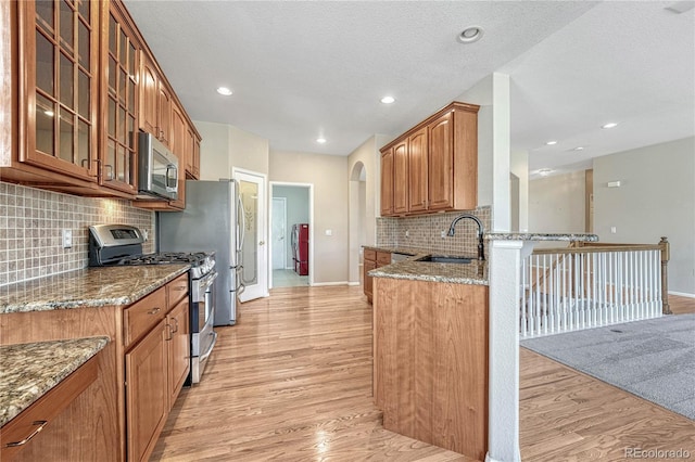 kitchen featuring light wood finished floors, stone countertops, a sink, glass insert cabinets, and appliances with stainless steel finishes