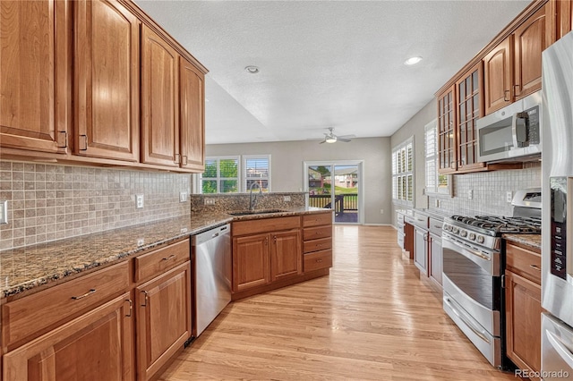 kitchen with brown cabinets, light wood-style flooring, a sink, stainless steel appliances, and ceiling fan