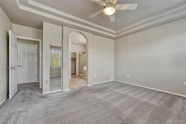 unfurnished bedroom with a tray ceiling, ensuite bath, arched walkways, carpet floors, and baseboards