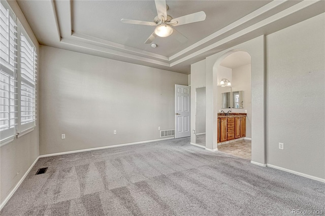 unfurnished bedroom with visible vents, baseboards, a tray ceiling, carpet floors, and arched walkways