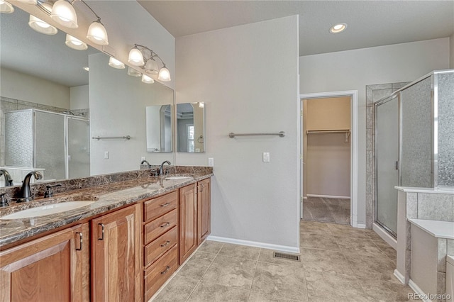 full bath featuring a walk in closet, a shower stall, double vanity, and a sink