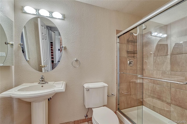 bathroom with toilet, a textured wall, a stall shower, and a textured ceiling