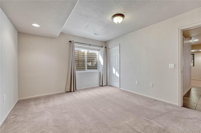 carpeted empty room featuring visible vents, a textured wall, baseboards, and a textured ceiling