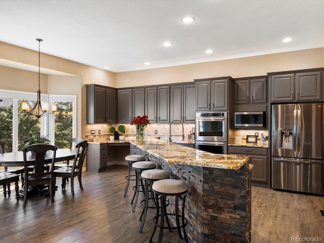 6266 W Prentice Ave, Littleton, CO 80123 - kitchen featuring a sink, stainless steel appliances, light stone counters, an island with sink, and an inviting chandelier