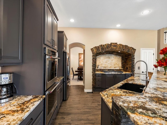 6266 W Prentice Ave, Littleton, CO 80123 - kitchen featuring light stone counters, dark wood finished floors, a sink, arched walkways, and stainless steel appliances