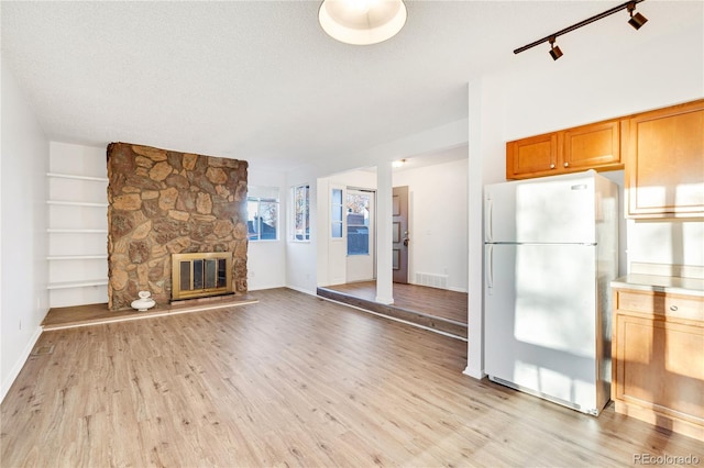 unfurnished living room with a textured ceiling, light wood-type flooring, track lighting, and a stone fireplace