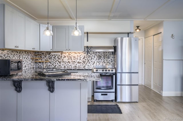 kitchen featuring stainless steel appliances, tasteful backsplash, a sink, dark stone counters, and a kitchen bar