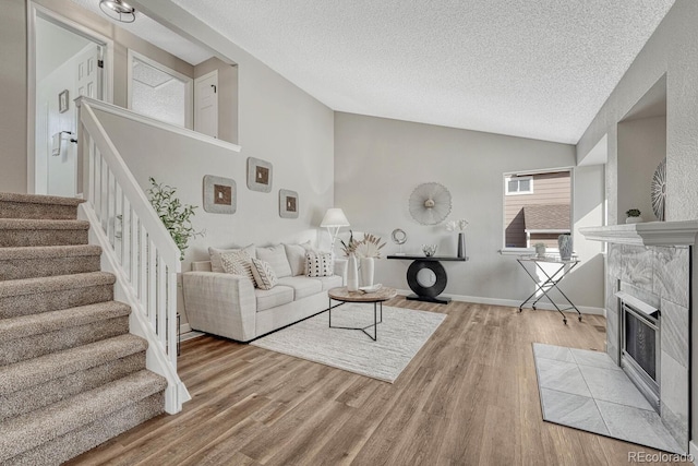 living room featuring lofted ceiling, a fireplace, stairs, and light wood-style flooring