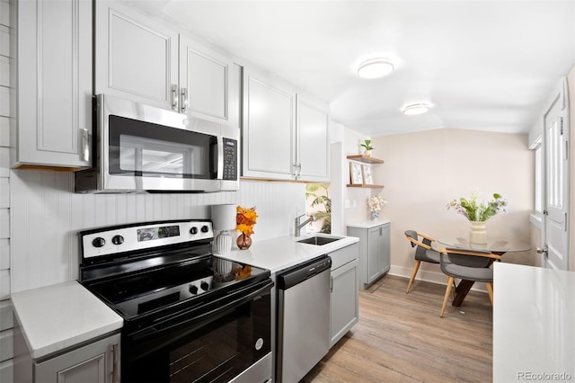 kitchen featuring appliances with stainless steel finishes, light wood-type flooring, sink, and lofted ceiling