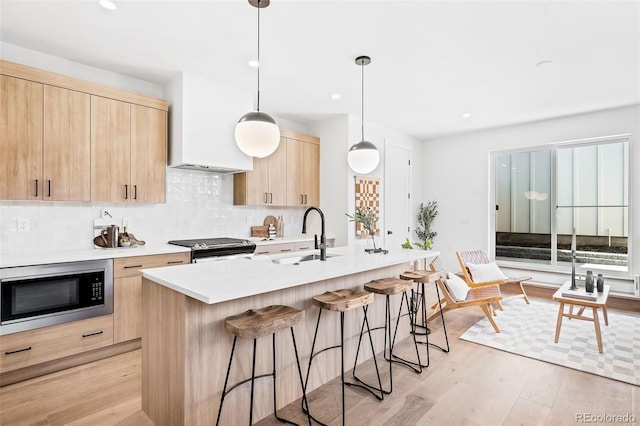 kitchen with pendant lighting, stainless steel appliances, light brown cabinetry, light hardwood / wood-style floors, and a kitchen island with sink