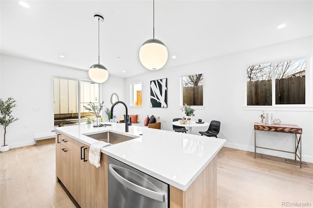 kitchen featuring decorative light fixtures, a center island with sink, stainless steel dishwasher, sink, and light brown cabinets