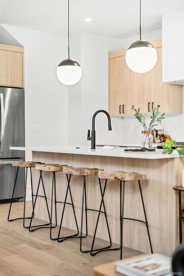 kitchen featuring light hardwood / wood-style floors, pendant lighting, stainless steel fridge, and light brown cabinetry