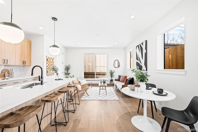 kitchen with light hardwood / wood-style floors, a kitchen breakfast bar, light brown cabinetry, hanging light fixtures, and sink