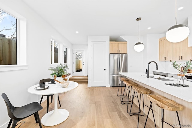 kitchen featuring light hardwood / wood-style floors, light brown cabinets, decorative light fixtures, stainless steel refrigerator, and sink