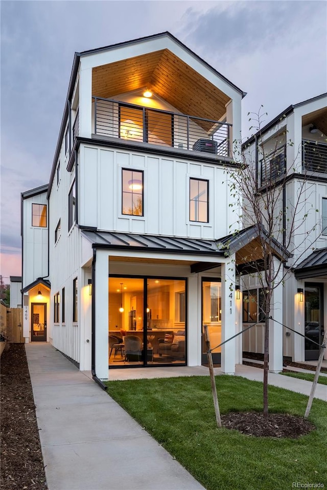 back house at dusk featuring a lawn and a balcony