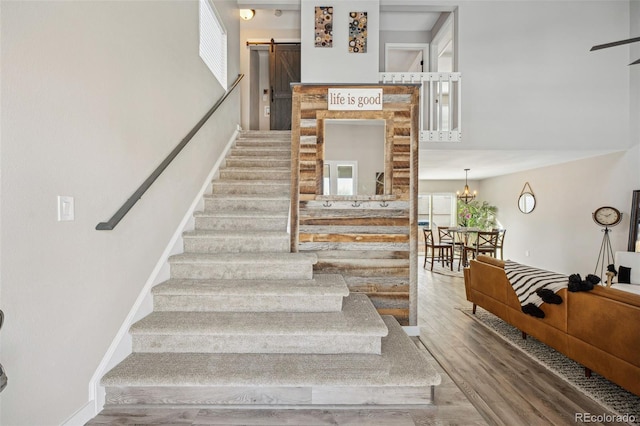 stairs with an inviting chandelier, hardwood / wood-style floors, a barn door, and a high ceiling