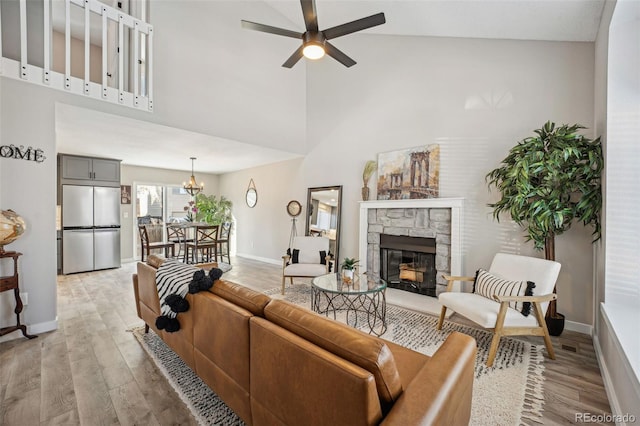 living room featuring a fireplace, ceiling fan with notable chandelier, light hardwood / wood-style flooring, and high vaulted ceiling