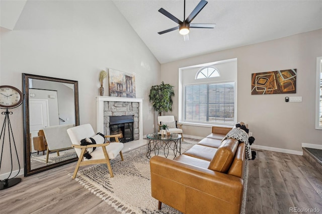 living room featuring hardwood / wood-style floors, a stone fireplace, high vaulted ceiling, and ceiling fan