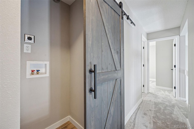 corridor with light carpet, a barn door, and a textured ceiling