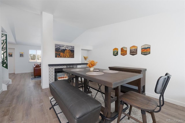 dining space featuring a warm lit fireplace, vaulted ceiling, baseboards, and wood finished floors