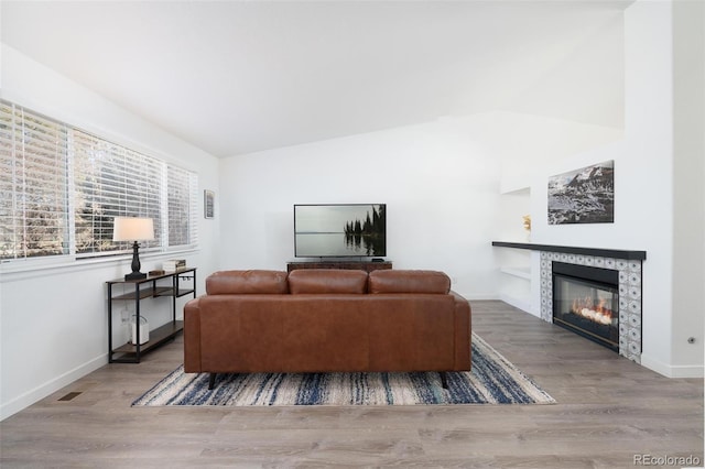 living room featuring lofted ceiling, a tile fireplace, wood finished floors, and baseboards