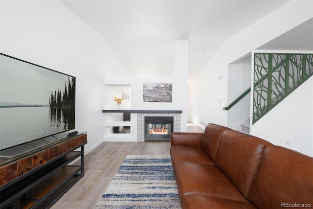 living area with baseboards, wood finished floors, stairs, vaulted ceiling, and a fireplace