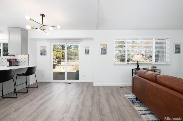 living room with light wood-style flooring, visible vents, a chandelier, and baseboards