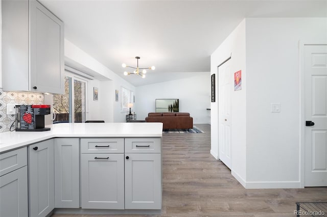 kitchen with lofted ceiling, light wood-style flooring, a peninsula, light countertops, and backsplash