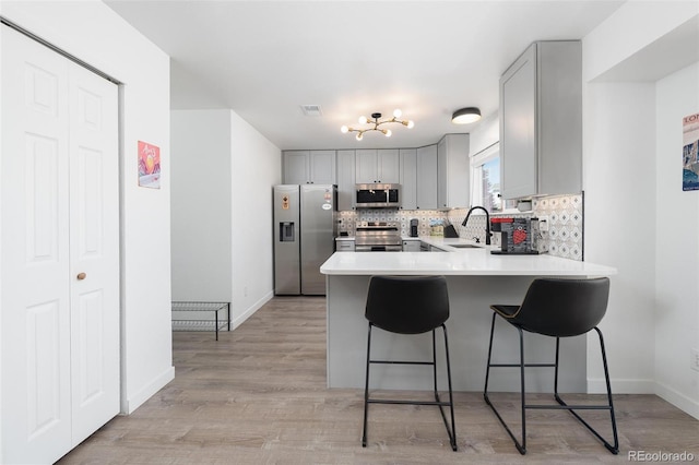 kitchen with a peninsula, gray cabinets, stainless steel appliances, and a sink