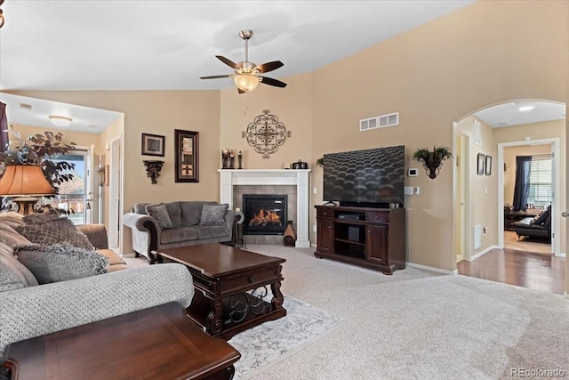 living area featuring ceiling fan, arched walkways, carpet, a tile fireplace, and visible vents